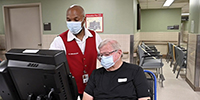 Army Veteran and Red Coat Ambassador Joe Buais helps a Veteran check in for an appointment